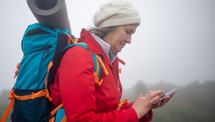 Wanderin mit großem Rucksach bedient ihr Smartphone im Nebel